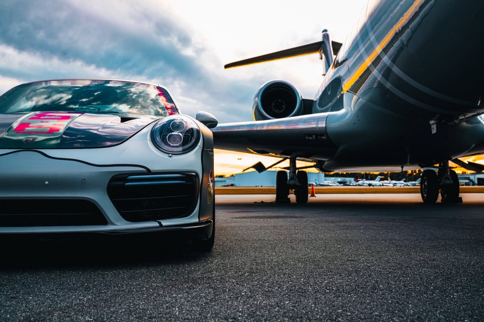 Silver Porsche parked beside a private jet at sunset