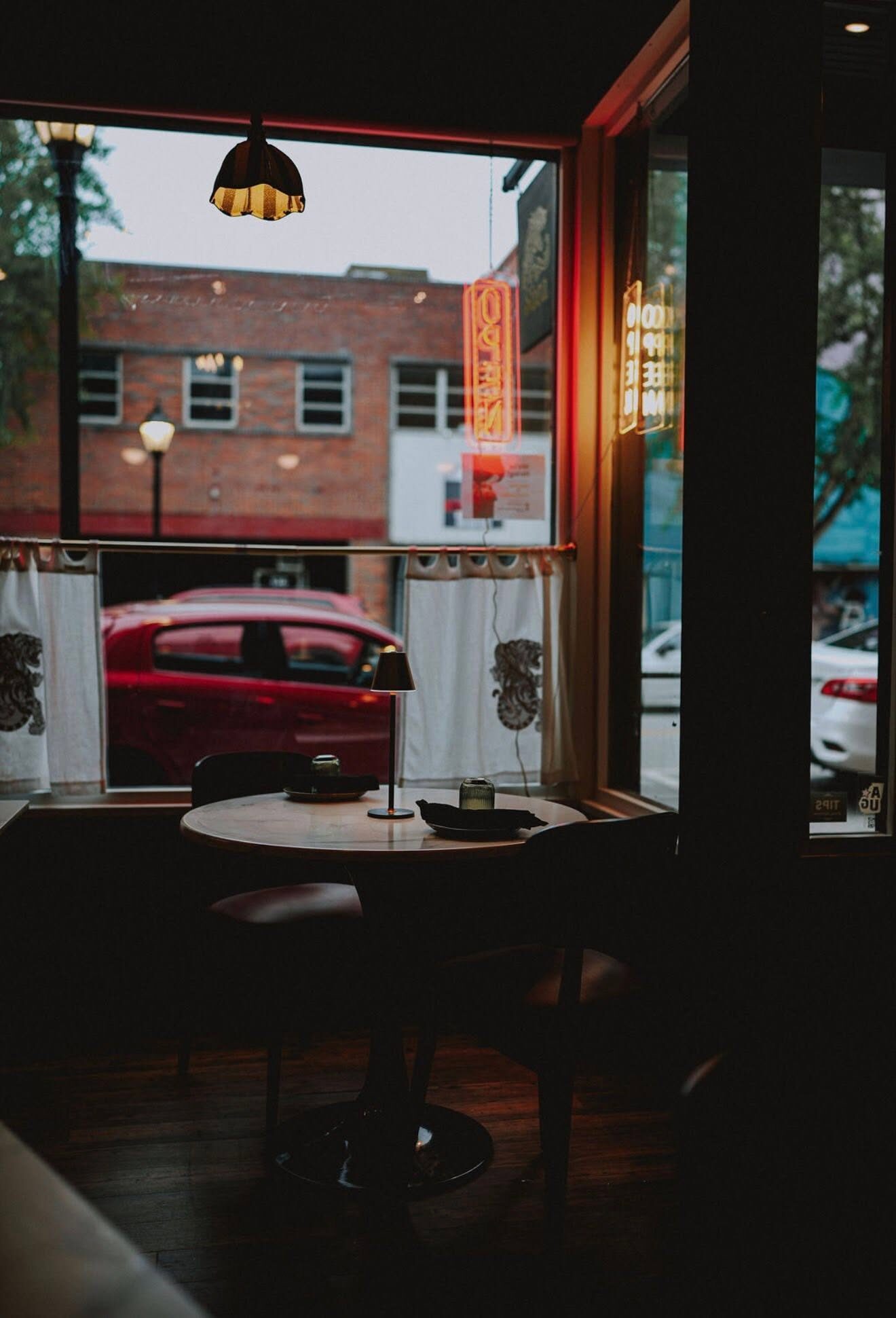 Moody cafe window table with neon signs at dusk
