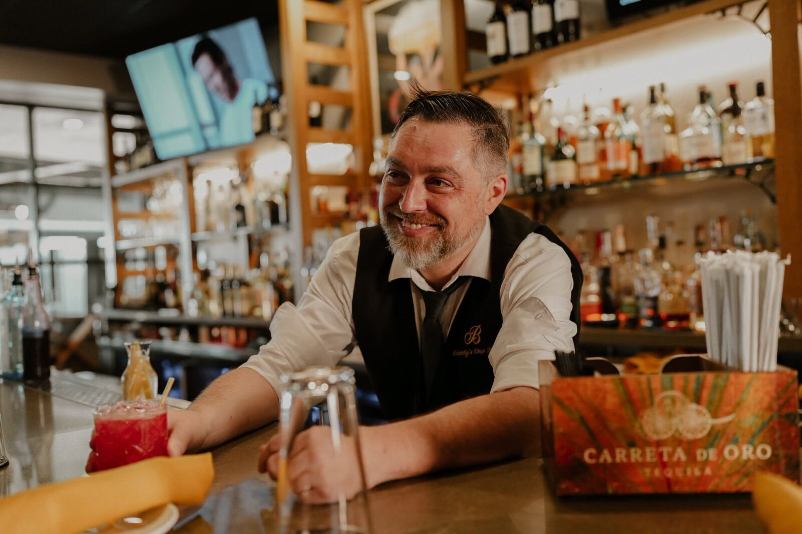 Smiling bartender leaning on the bar in front of backlit bottles