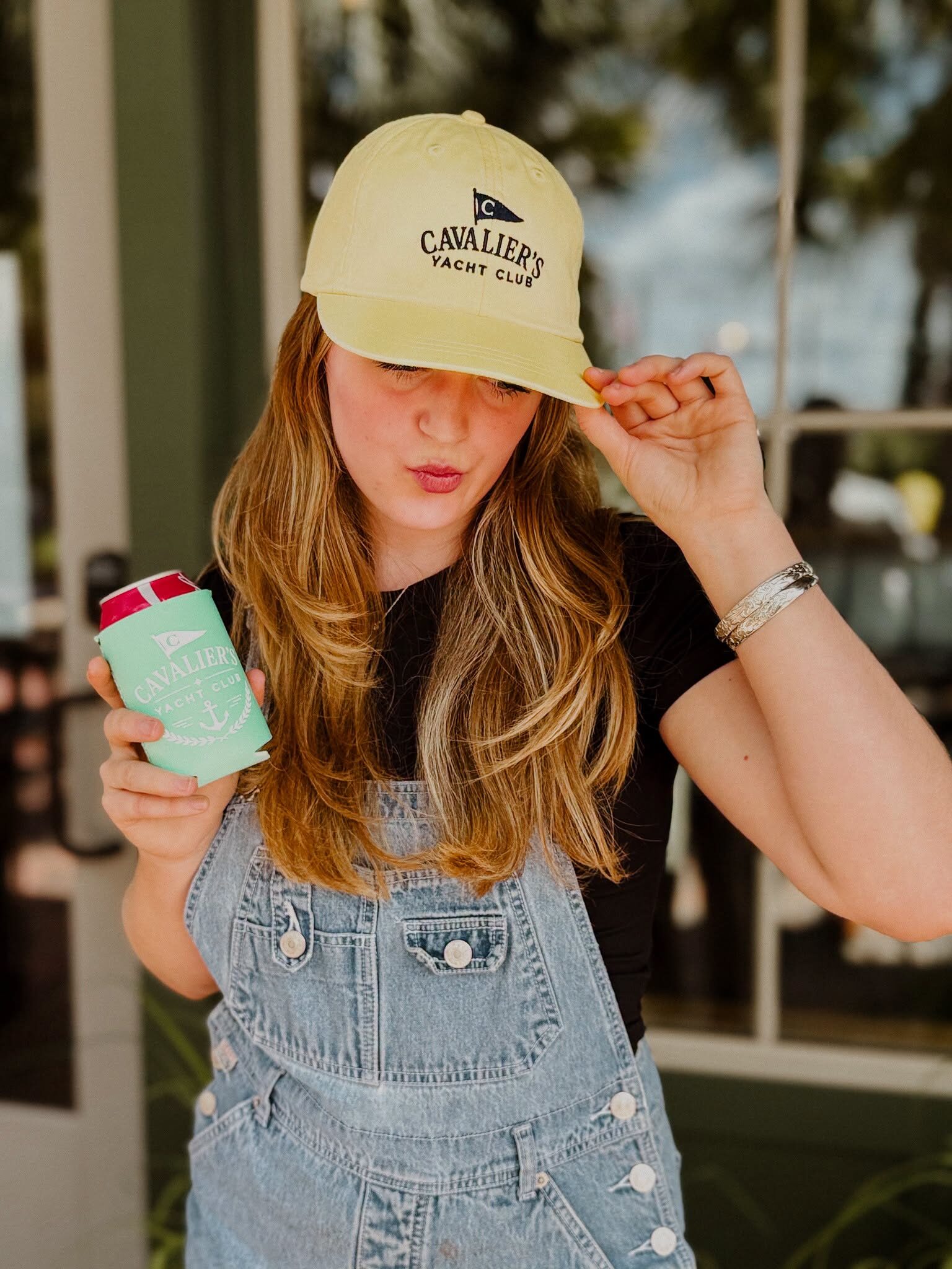 Model in a yellow Cavalier's Yacht Club cap holding a matching koozie