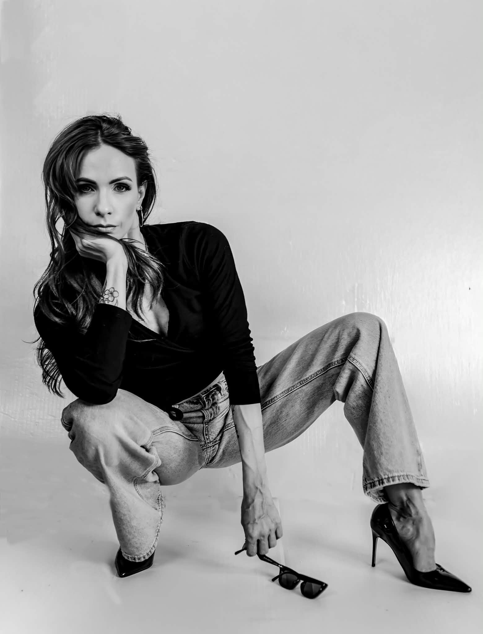 Black-and-white studio portrait of a woman crouched on the floor in heels