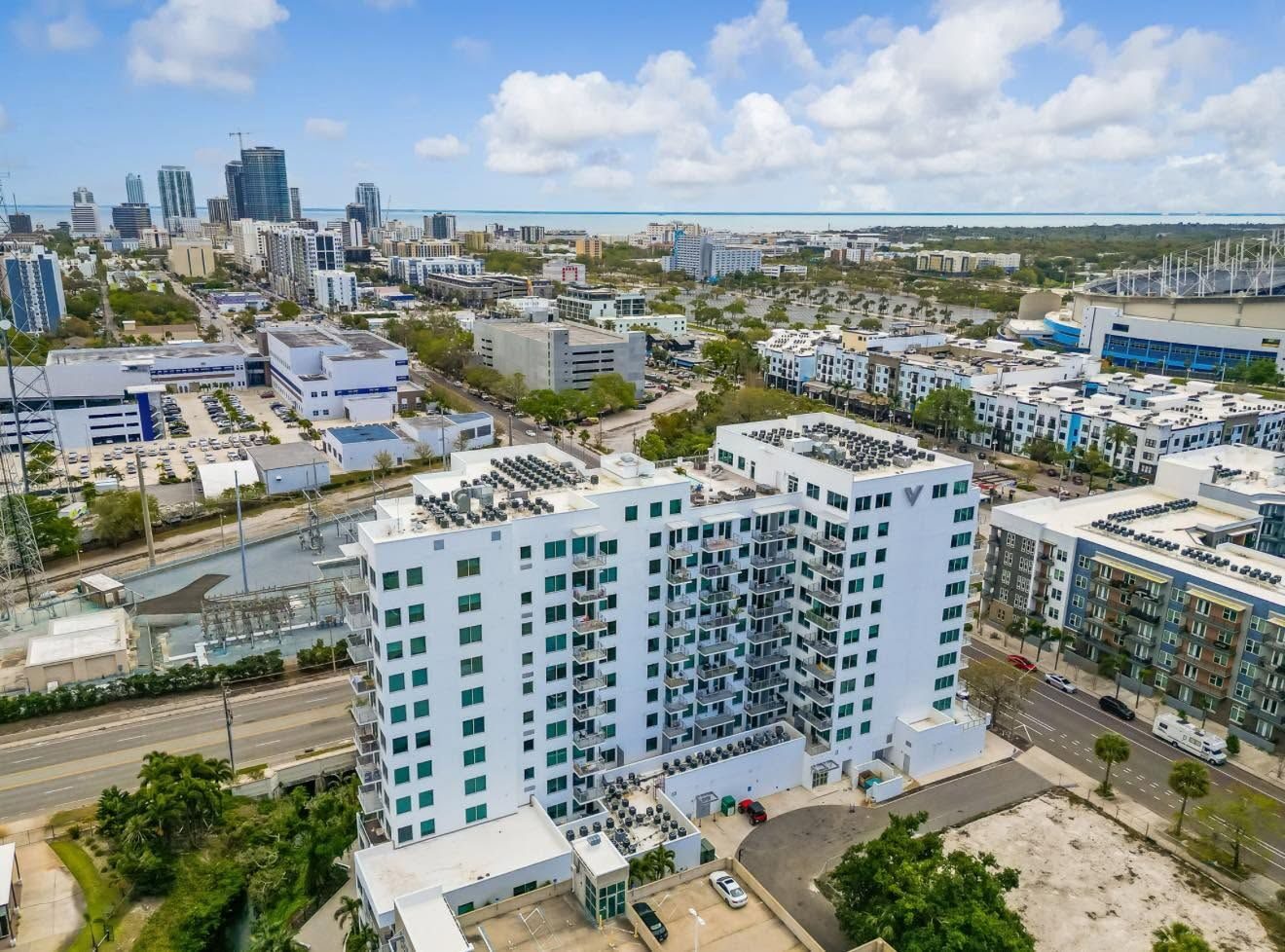 Aerial view of a white high-rise with the downtown skyline and bay behind it
