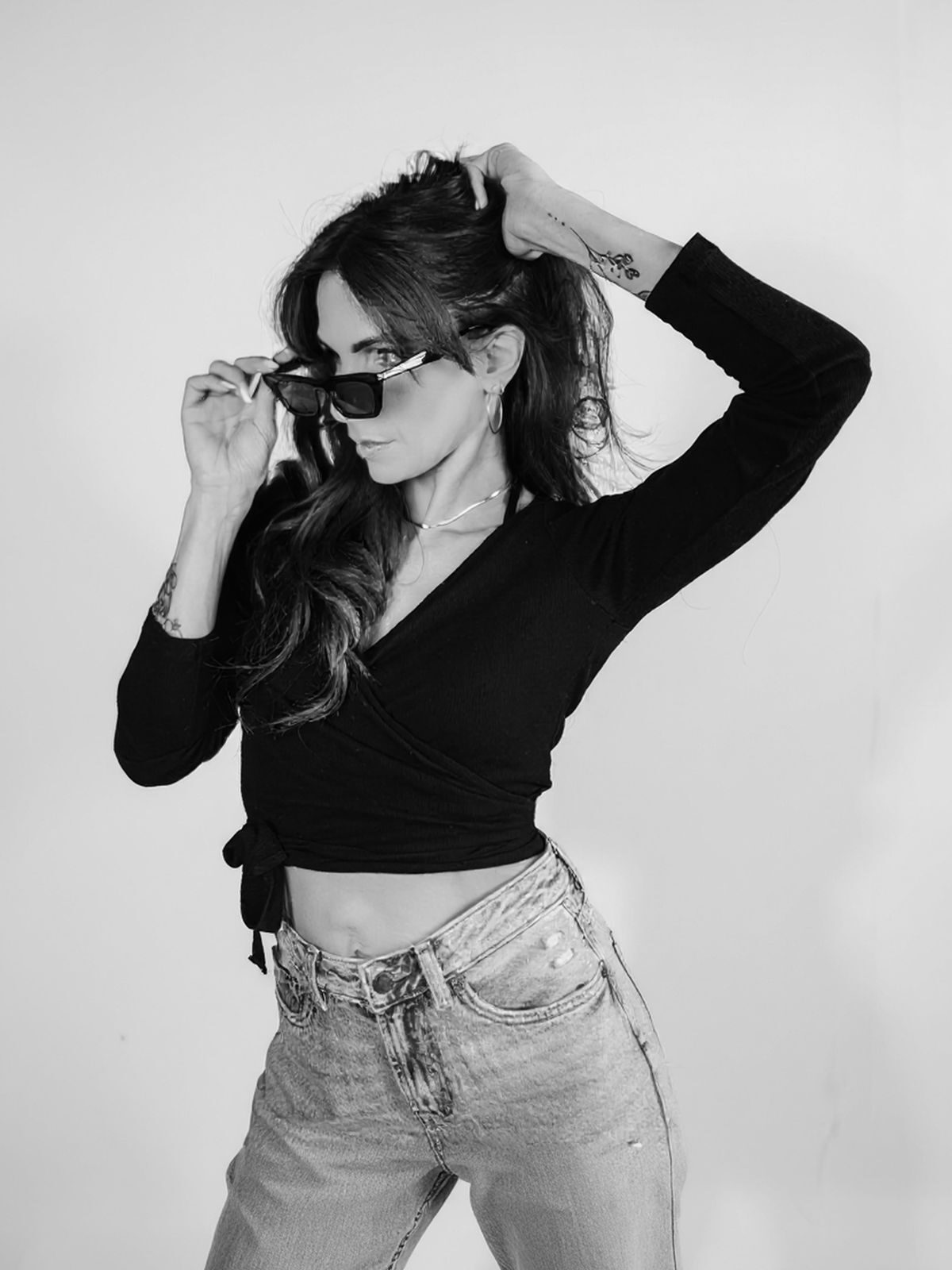 Black-and-white studio portrait of a model lowering her sunglasses