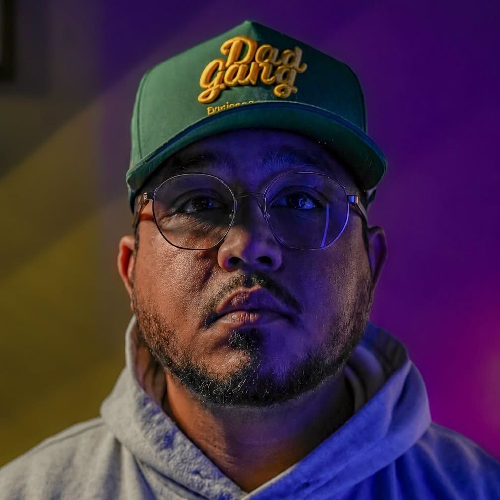 Mikey Cruz in a green cap and glasses under purple studio light