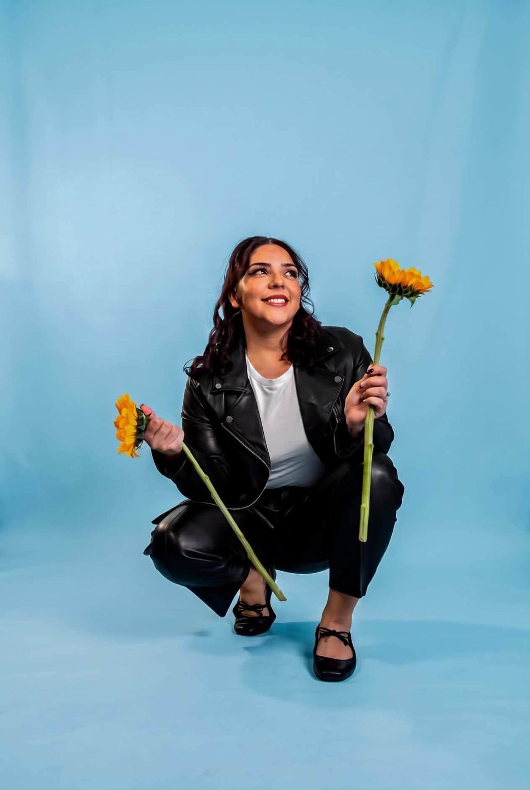 Studio portrait of a woman in a leather jacket holding sunflowers on a blue backdrop